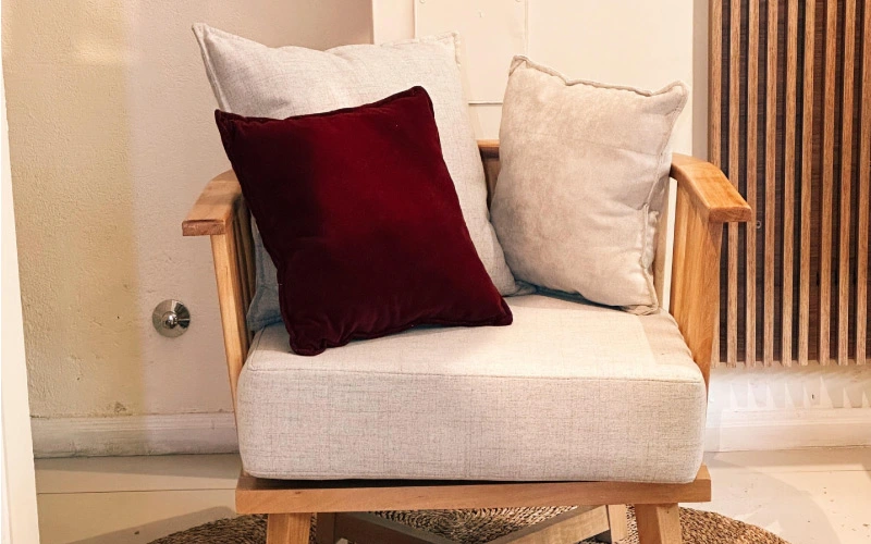 Sillón de estructura de madera con asiento tapizado en lino claro y almohadones