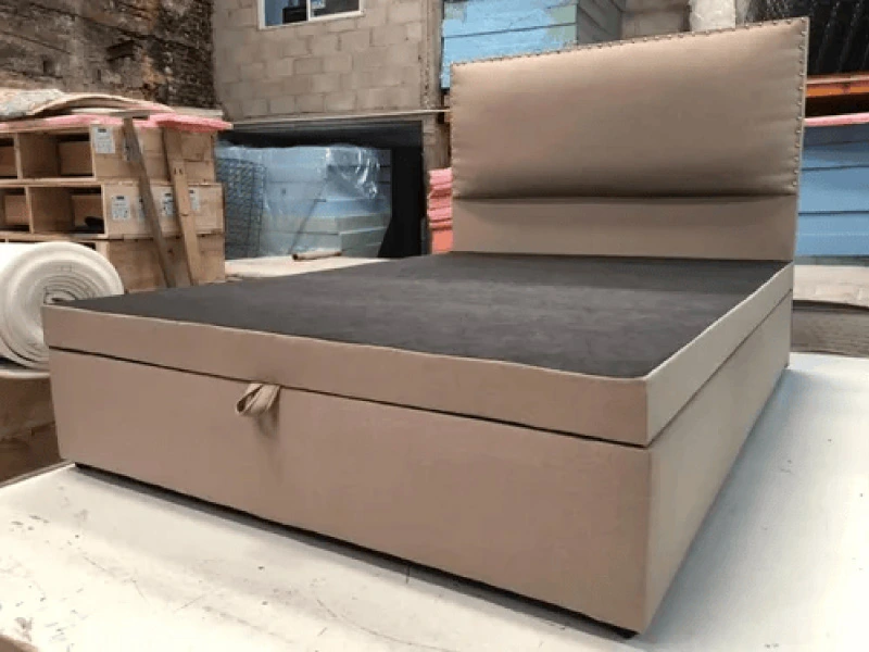 Base de cama tapizada en tela beige con respaldo y tapa levantada
